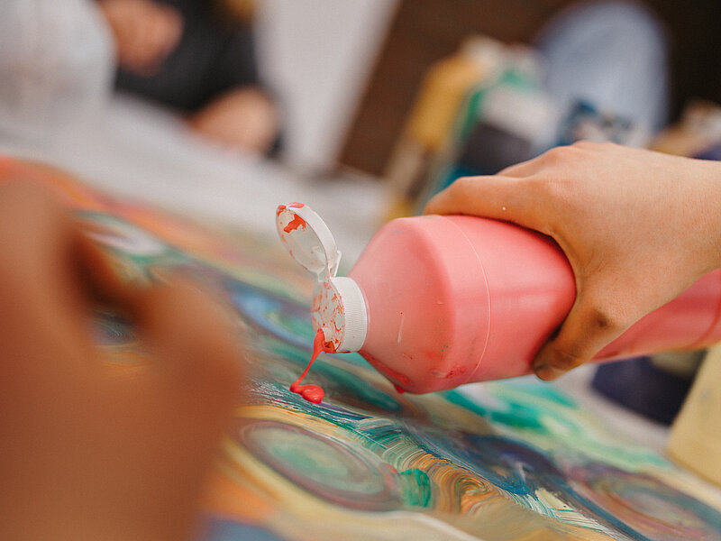 Hand kippt Farbe auf Leinwand
